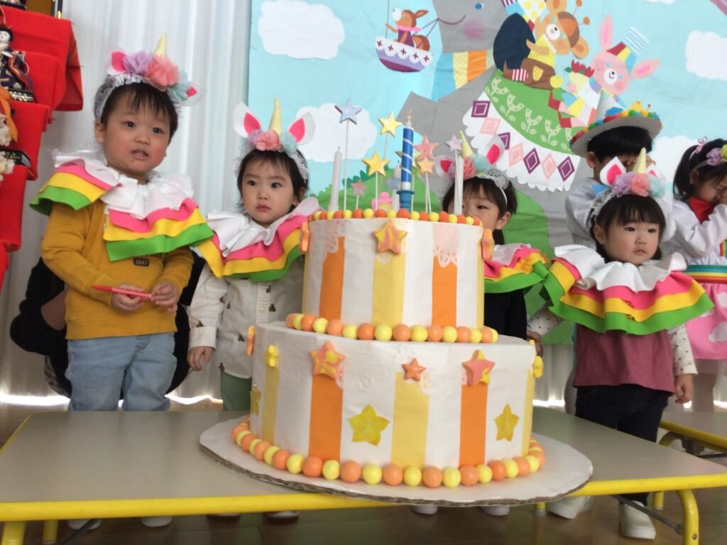 誕生ケーキの後ろで願い事をする誕生児たち